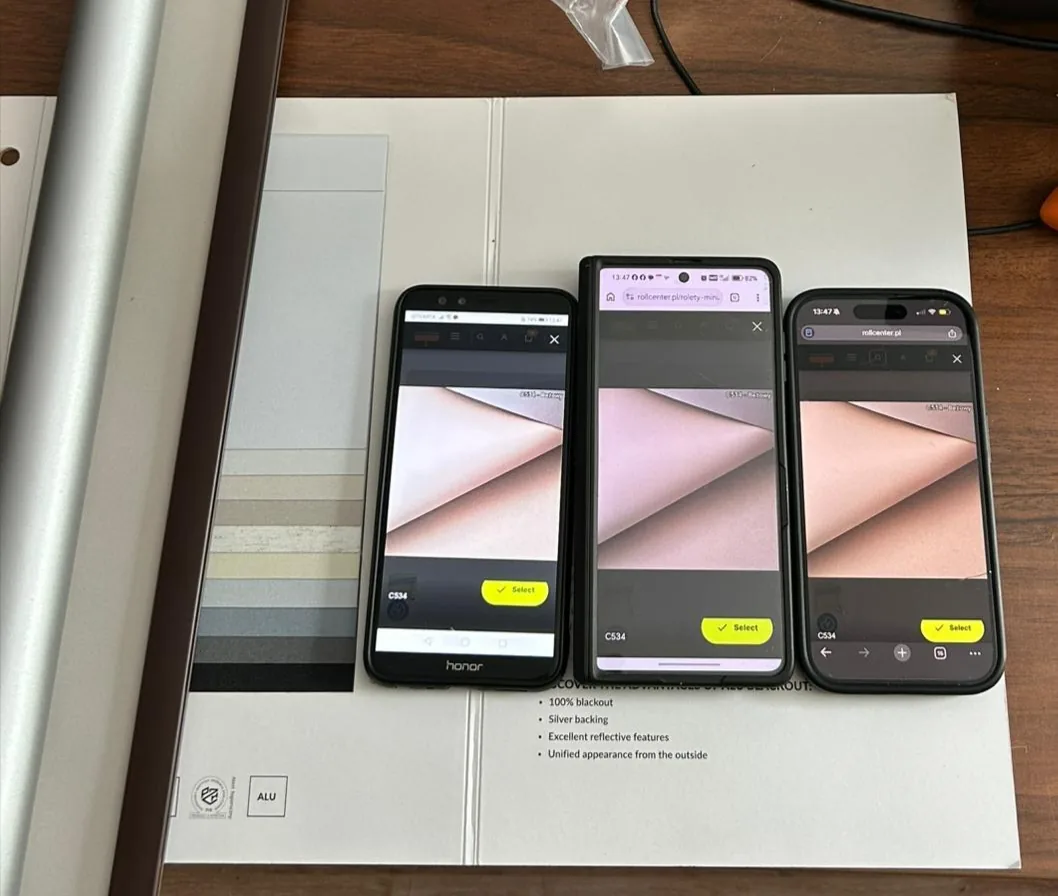 Tkanina C534 Beżowy na trzech telefonach różnych producentów leżących na wzorniku tkanin — każdy telefon pokazuje inny odcień